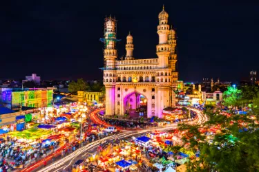 Illuminated Charminar monument in Hyderabad at night, surrounded by bustling markets